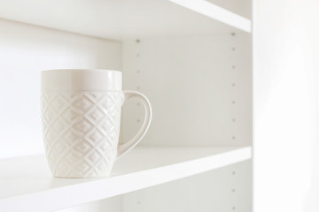 A white ceramic mug standing on an empty shelf.