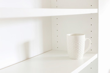 A white ceramic mug standing on an empty shelf.
