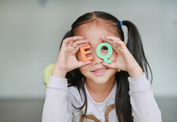 Cute little Asian child girl holding alphabet EQ (Emotional Quotient) text on her face. Education...