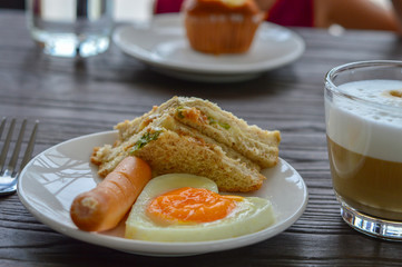 Breakfast on the table has fried eggs, sausages, sandwiches and coffee.