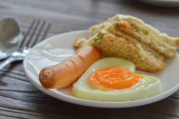 Breakfast on the table has fried eggs, sausages, sandwiches.