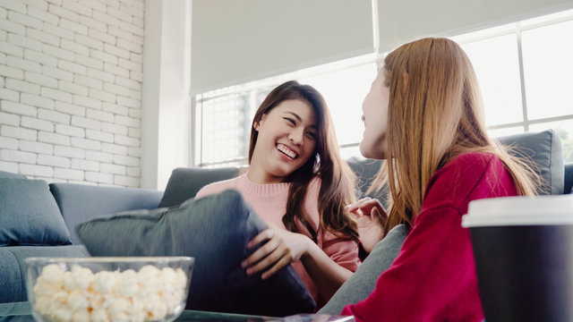 Asian Women Playing Pillow Fight And Eating Popcorn In Living Room At Home, Group Of Roommate Friend Enjoy Funny Moment While Lying On The Sofa. Lifestyle Women Relax At Home Concept.