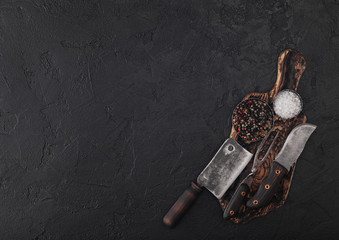 Vintage meat knife and fork on vintage chopping board and black stone table background. Butcher...