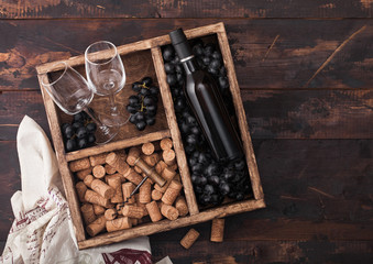 Luxury bottle of red wine and empty glasses with dark grapes with corks and corkscrew inside vintage wooden box on dark wooden background with linen towel.Top view
