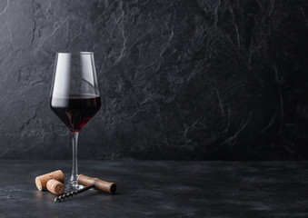 Elegant glass of red wine with corks and corkscrew on black stone background. Natural Light