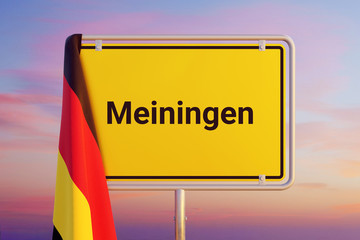 Meiningen. Gelbes Schild/Ortsschild. Flagge von Deutschland hängt darüber. Himmel mit Sonnenuntergang oder Sonnenaufgang