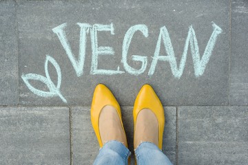 Female feet with text vegan written on grey sidewalk