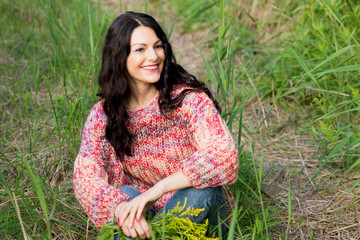 The woman in a knitted pullover poses against the background of the nature