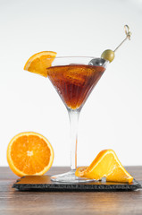Dark alcoholic cocktail with slices of ripe lemon and olives on a wooden table and a white background - Ripe lemon and green and black olives