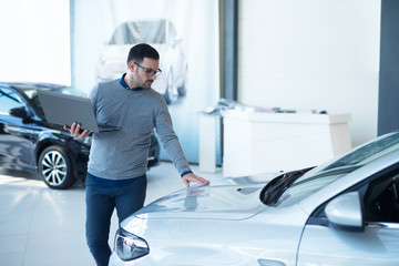 Car salesperson with laptop checking vehicle specifications in local dealership showroom. Vehicle...