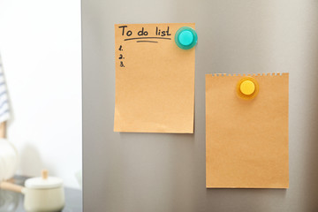 To do list and empty sheet of paper with magnets on refrigerator door in kitchen. Space for text