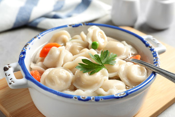 Bowl of tasty dumplings in broth on table, closeup