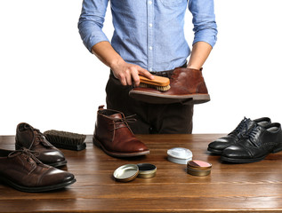 Man cleaning leather shoe at wooden table against white background, closeup