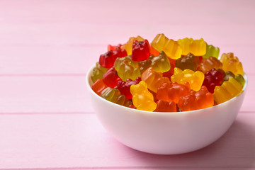 Bowl with delicious bright jelly bears on pink wooden table, space for text