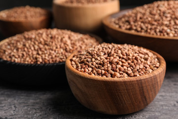 Wooden bowls full of uncooked buckwheat on grey table