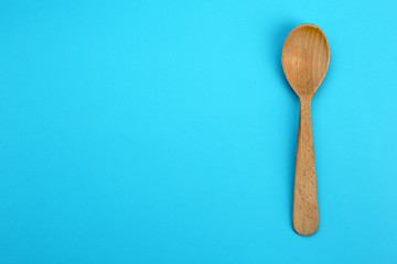 Clean empty wooden spoon on blue background, top view. Space for text