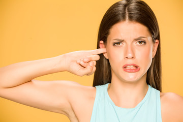 Beautiful young woman with with finger in her ear on yellow background