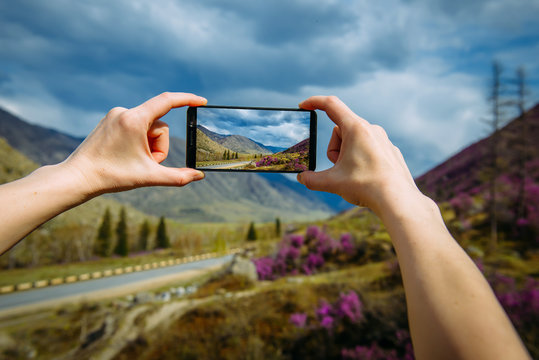Close-up of hands taking photo or video on the smartphone. Unknown person shoots a stunning mountain landscape on a cloudy day. Focus on the gadget screen, blurred background. Travel blog.