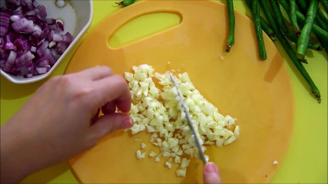 Overhead or flatlay steady video shot of a person mincing garlic with a knife on a chopping board
