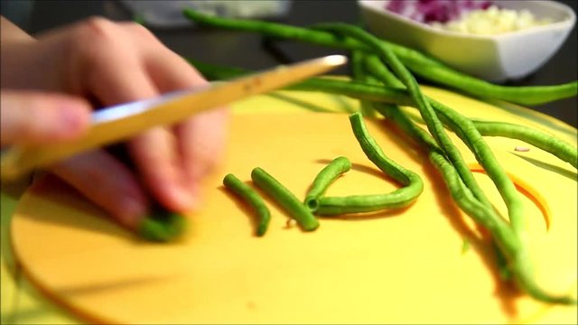 Close up steady video shot of a person cutting or slicing string beans with a knife on a chopping board