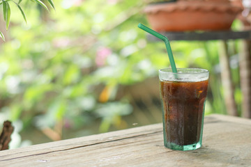 Cup of iced black coffee (Americano) on wood table with garden view.