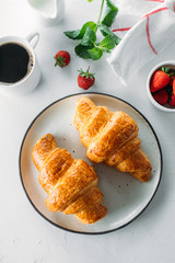 Breakfast concept. Cup of coffee, freshly baked croissants and fresh strawberry on wooden table background. Top view
