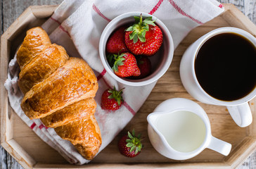 Breakfast concept. Cup of coffee, freshly baked croissants and fresh strawberry on wooden tray. Wooden table background. Top view, close-up