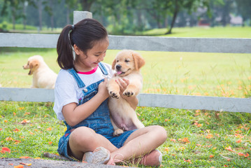 Young asian girl playing with a little golden retriever dog in park