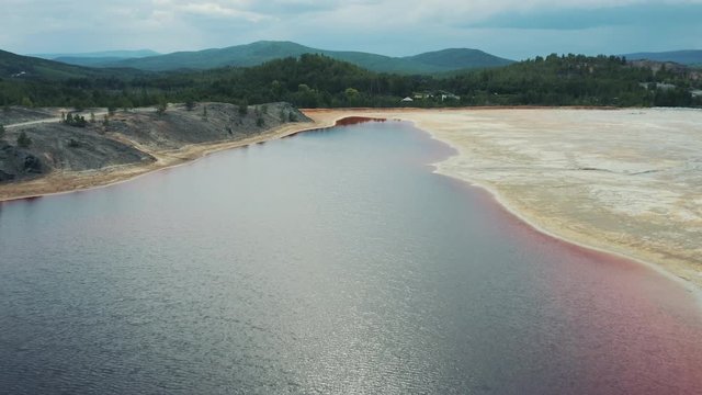 Pink colored water reservoir; copper digging production site; contamination territory, ecological catastrophe; drone flying over a water surface; aerial industrial landscape, anthropogenic influense