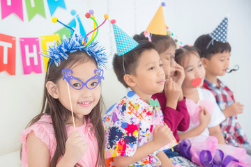 Little asian girl holding eyeglasses ,party accessory with friends at birthday party
