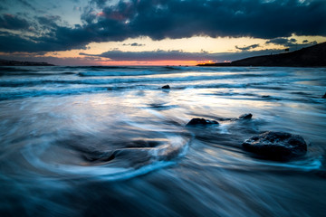 Obraz premium Cold coloured dramatic beautiful sunrise at the beach with ocean stretch waves and great sky with clouds. Long exposure water effect and nobody out there - wild outdoor nature