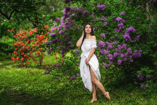 photo of young woman walking through lilac garden in bloom.Outdoor . Barefoot.