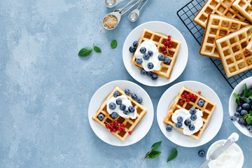 Traditional belgian waffles with cream cheese and fresh blueberry on blue background, top view