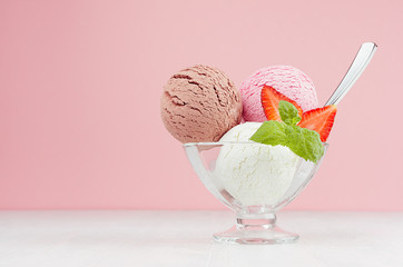 Seasonal sweet dairy dessert - ice cream scoops different flavor with spoon, strawberry slices, mint in elegant bowl in modern stylish pastel pink interior.