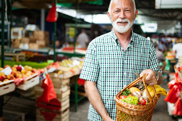 Positive elderly man buying seasonal vegetables in local market