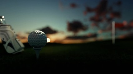 Golf clubs and golf ball on tee with red flag against beautiful timelapse sunrise, tilt