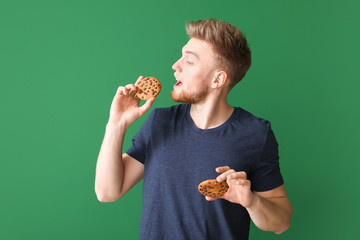 Handsome young man with tasty cookies on color background