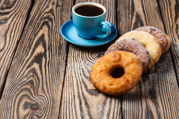 Many homemade baked donuts without cream sprinkled of powdered sugar near full cup of hot black coffee lies on old rustic wooden table
