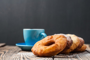 Many homemade baked donuts without cream sprinkled of powdered sugar near full cup of hot black coffee lies on old rustic wooden table