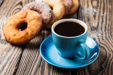 Many homemade baked donuts without cream sprinkled of powdered sugar near full cup of hot black coffee lies on old rustic wooden table