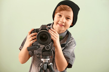 Cute little photographer with professional camera on color background