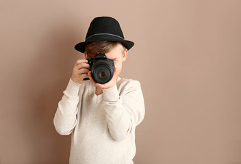 Cute little photographer with professional camera on color background