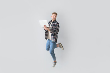 Jumping young man with laptop on light background