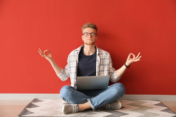 Handsome young man with laptop meditating near color wall