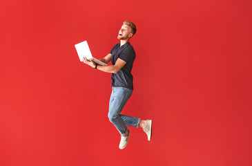 Jumping young man with laptop on color background