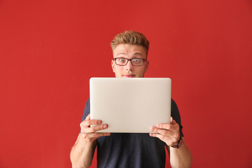 Shocked young man with laptop on color background