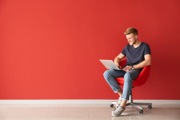 Handsome young man with laptop sitting on chair near color wall - Powered by Adobe