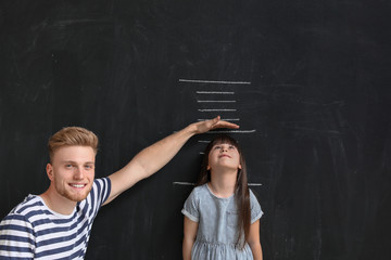 Father measuring height of his little daughter near wall with marks