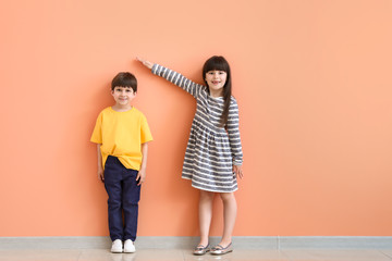 Cute little children measuring height near color wall - obrazy, fototapety, plakaty