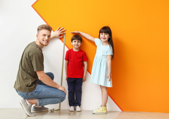 Father and his little children measuring height near wall